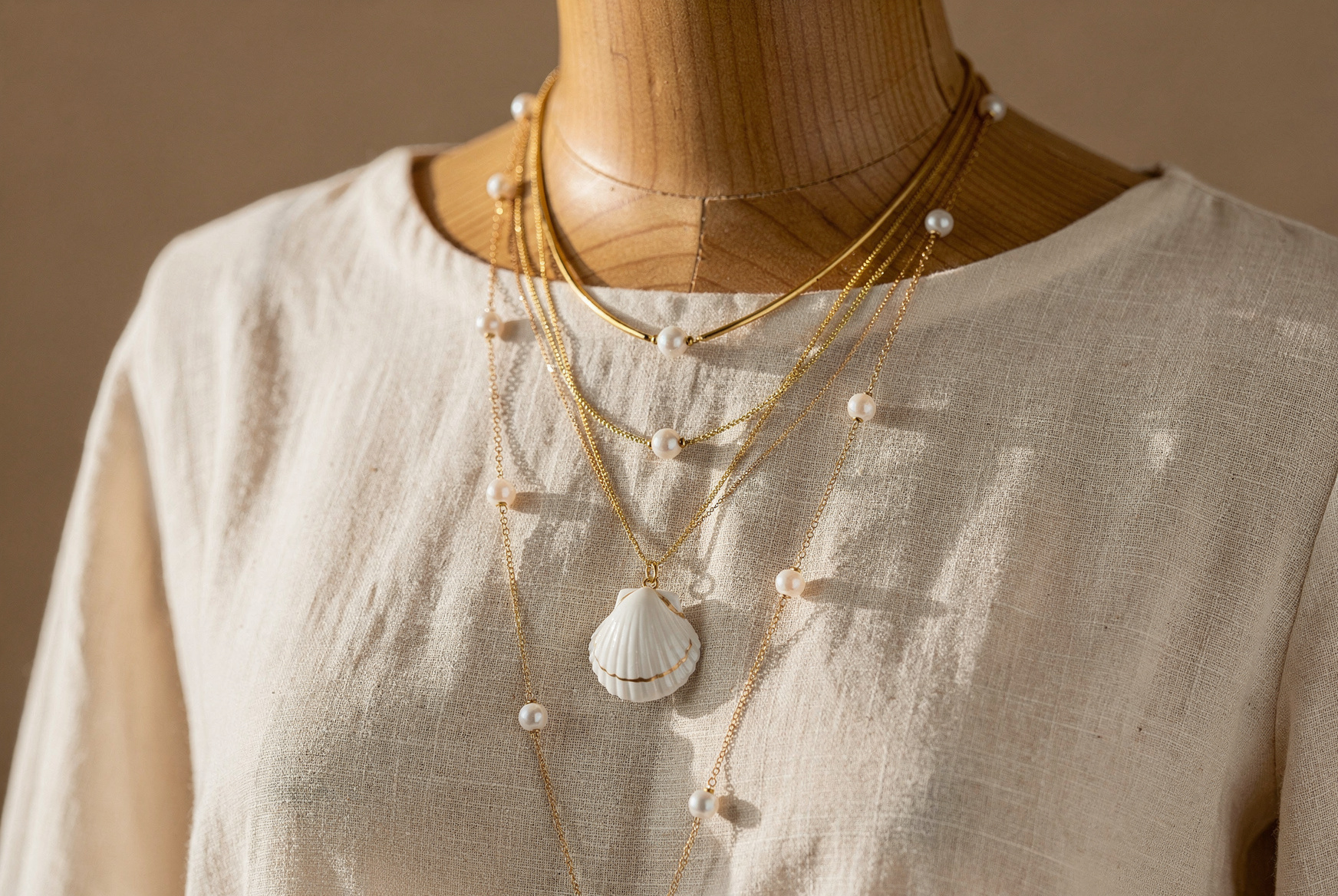 Superposition de colliers bohèmes dorés avec pendentif coquillage en porcelaine sur une robe en lin écru