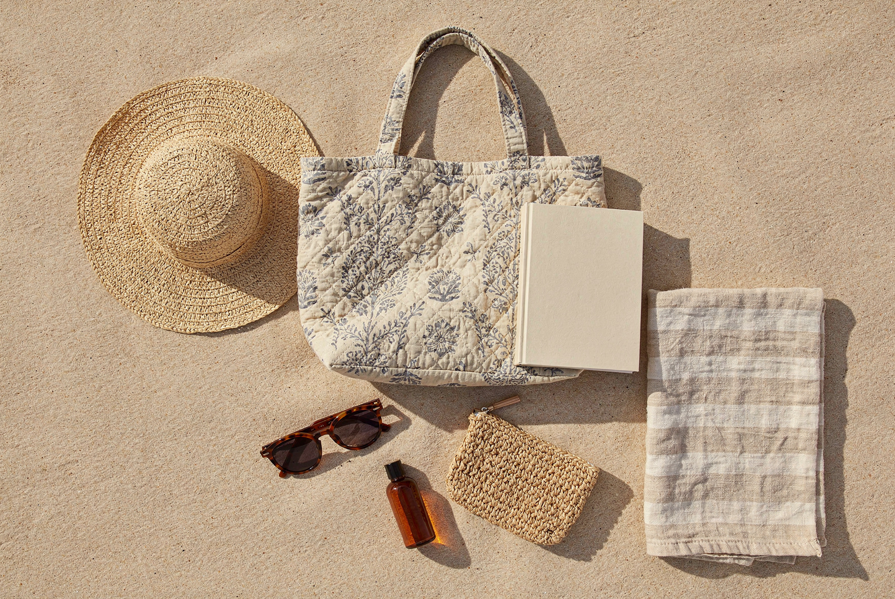 Sac cabas en coton matelasse a imprime block print pose sur le sable avec un chapeau de paille, des lunettes de soleil, un drap de plage et une pochette