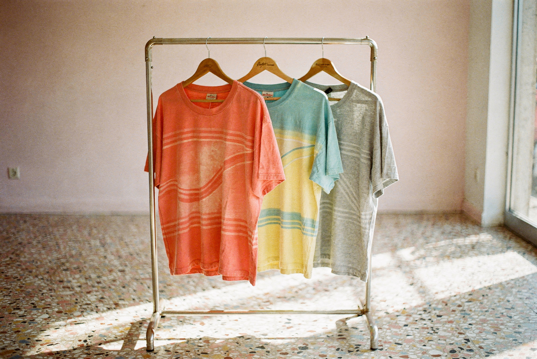 Portant vintage avec trois tee-shirts années 80 surf californien corail, turquoise et gris dans une boutique lumineuse