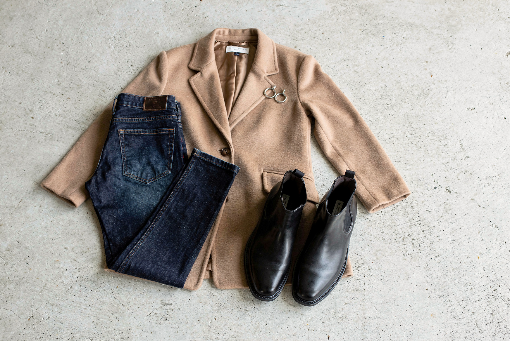 Bottines chelsea en cuir noir posées à plat avec un jean droit, un manteau camel et des créoles argentées